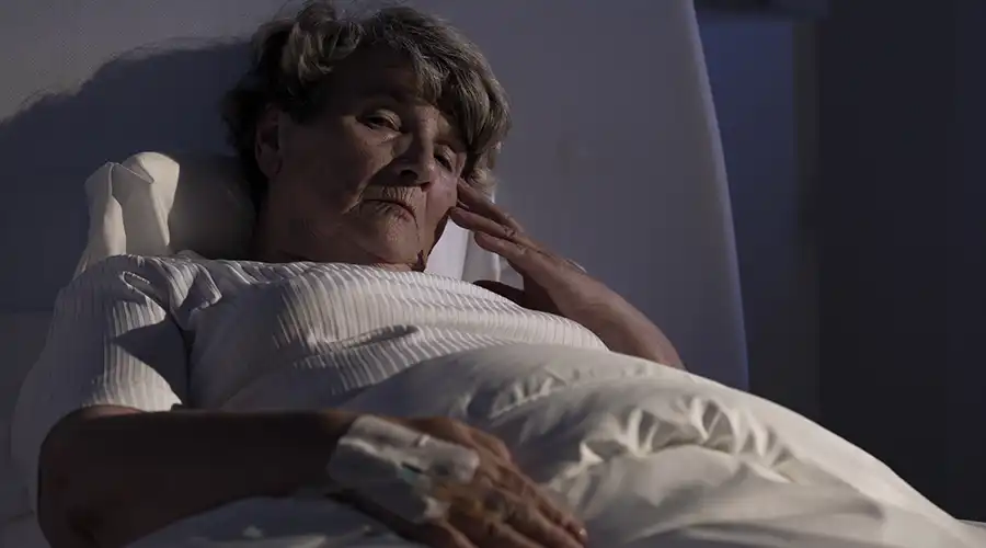 A woman lying in a hospital bed, holding her head with her hand, possibly experiencing discomfort or pain.