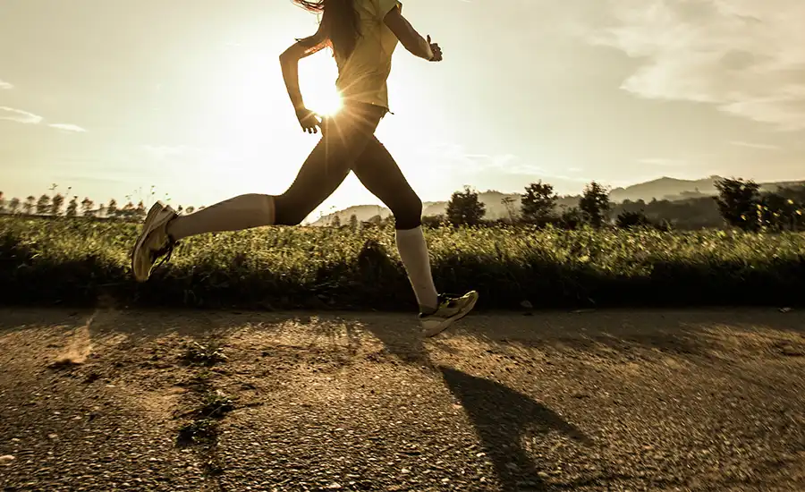 A woman jogging on a road during sunset, with the warm glow of the sun in the background.