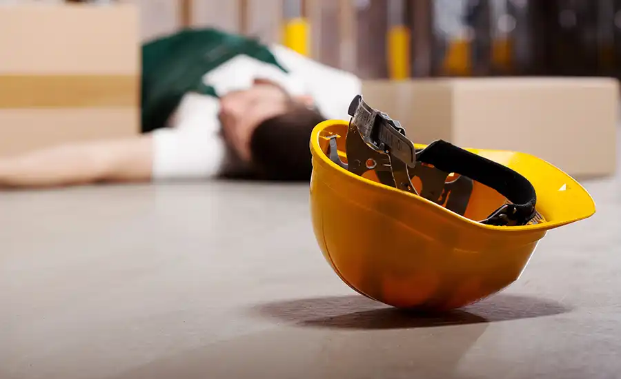 A man lying on the floor with a hard hat on the ground, depicting workplace injury complexities.