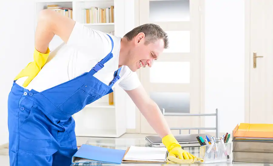 An individual wearing overalls and rubber gloves experiencing discomfort as he supports his back.