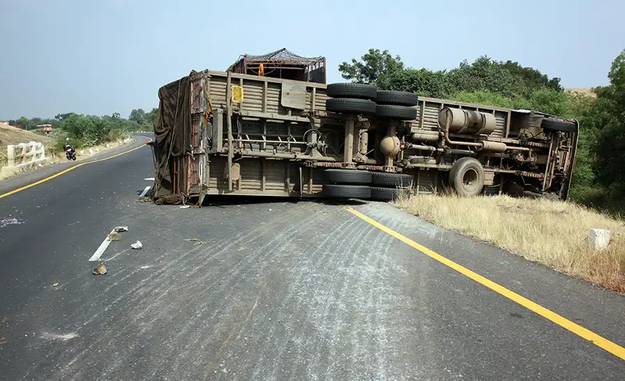 An overturned truck on the side of the road, surrounded by debris and emergency vehicles.