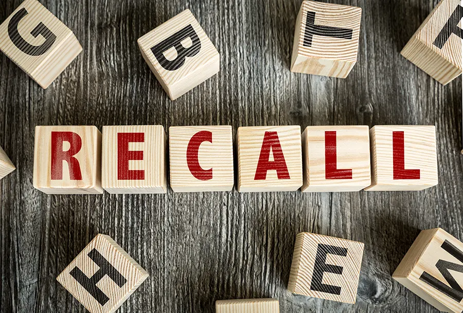 Wooden blocks on a rustic table spelling out the word 'recall,' surrounded by other scattered alphabet blocks.